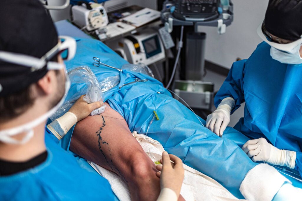 Médecin et chef de bloc opératoire procèdent à une microphlébectomie ambulatoire sur la jambe droite d'un patient couché